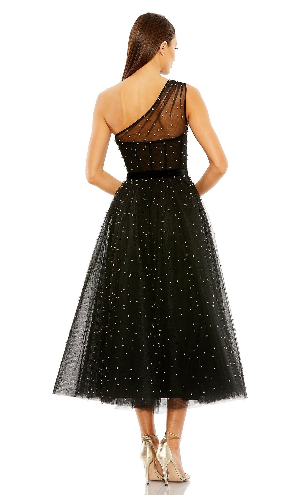 A woman faces away in the Mac Duggal 20745 Black Midi Wedding Guest Dress—an elegant one-shoulder tulle design with a sheer back and pearl accents—paired stylishly with strappy silver heels.